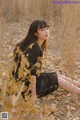 A woman in a black dress sitting in a field of dry grass.