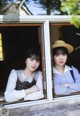 Two young women are looking out of a window.