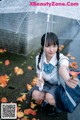 A woman in a school uniform holding an umbrella.