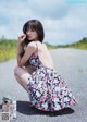 A woman in a floral dress sitting on the side of a road.